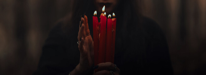 frightening witch performs an occult ritual with candles in a gloomy dark forest. Panoramic wide...