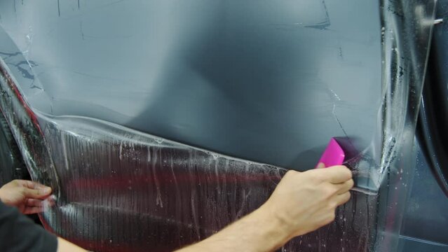 Process of applying a protective PPF film to a car. Hands of a professional applying a protective film of laminate. Close up shot