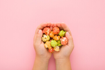 Sweet colorful popcorn in little child opened palms on light pink table background. Pastel color....