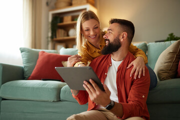 Handsome couple relaxing at home and looking at tablet - obrazy, fototapety, plakaty