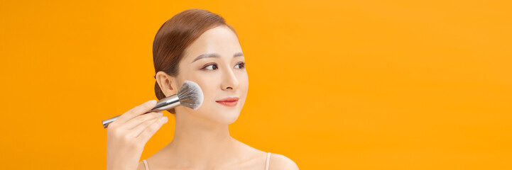 Young woman applies powder on the face using makeup brush. web banner.