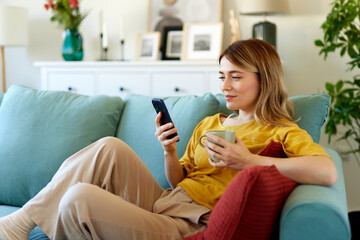 Woman using smartphone while drinking coffee at her home in the morning