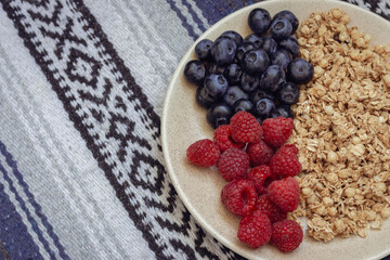 Muesli with blueberries and raspberries on tablecloth background. Granola with wild berries on towel pattern. Healthy eating. Bowl of oat flakes and blueberry and raspberry. Vitamin breakfast.