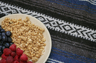 Muesli with blueberries and raspberries on tablecloth background. Granola with wild berries on towel pattern. Healthy eating. Bowl of oat flakes and blueberry and raspberry. Vitamin breakfast.