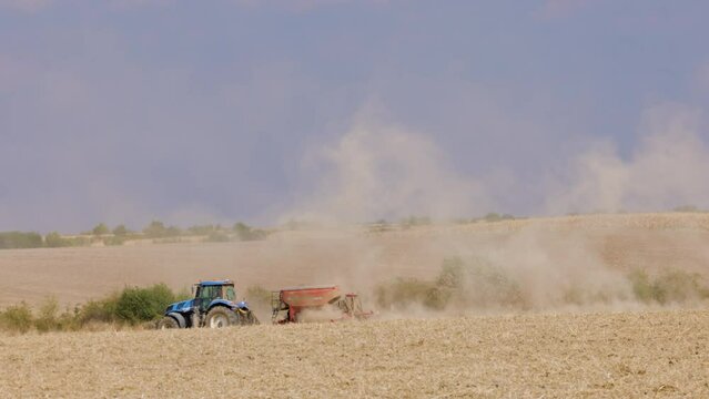 4k footage with an agricultural machine on a field that raises a lot of dust behind it.