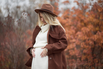 Profile image of a pregnant young woman with blonde hair, dressed in autumn clothes, posing in park.