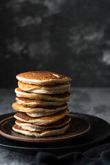 A stack of gluten-free, buckwheat pancakes in dark ceramic dishes in a dark style.