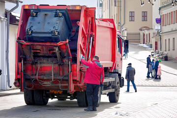 Refuse collector man unload dustbin in rear load garbage truck. Trash removal work in the city street, garbage truck loading waste from dustbins. Garbage removal in residential district.
