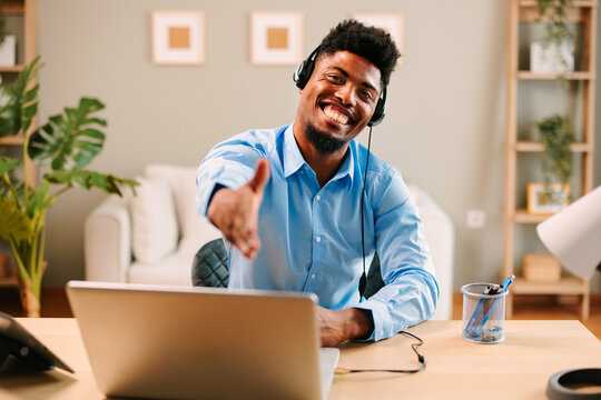 Customer support man with a smile on his face is sitting at a desk and extending his hand for a handshake