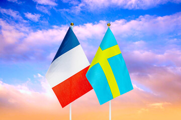 National flags of France and Sweden against the sky at sunset.