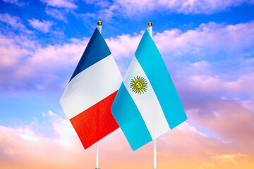 National flags of France and Argentina against the sky at sunset.