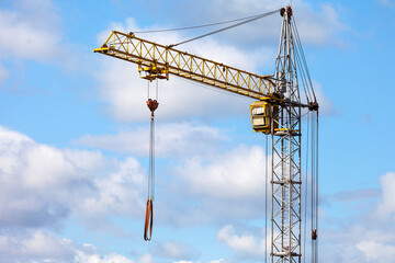 A high-rise construction crane against a background of blue sky with clouds. Residential urban construction and development concept