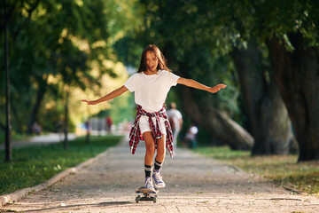 Controlling the balance. Happy little girl with skateboard outdoors © standret