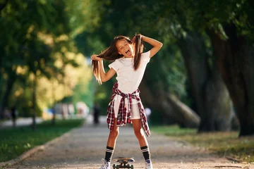 Poster Playing with the hair, going crazy. Happy little girl with skateboard outdoors © standret