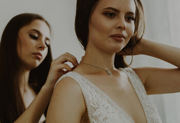 The bridesmaid helps to clasp the bride's necklace.