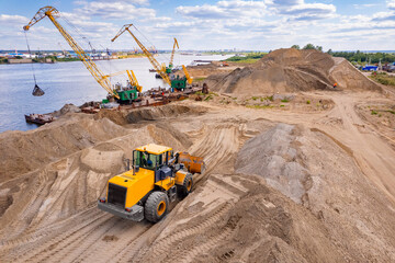 Aerial top view yellow excavator working on sand quarry, industrial crane unloads barge. Concept...