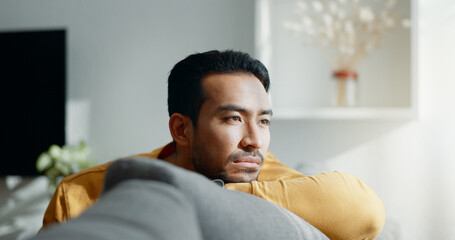 Thinking, memory and sad asian man on a sofa with nostalgia, depression or grief in his home....