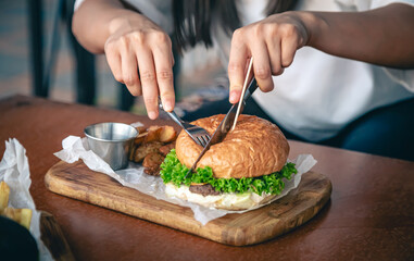 Close-up, a woman in a cafe cuts an appetizing burger.