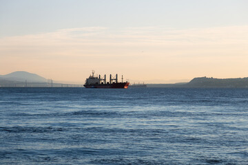 Obraz premium Cargo ships seen in the St. Lawrence River during a pink sunrise, with the Island of Orleans bridge in the background, Quebec City, Quebec, Canada