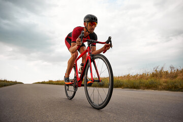 Competitive and concentrated man, triathlete riding bicycle on road outdoors, training for...