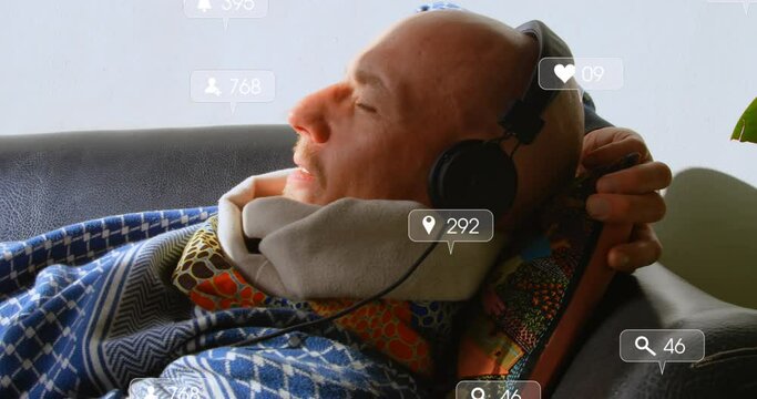Animation of social media icons over caucasian senior man listening to music lying on couch at home