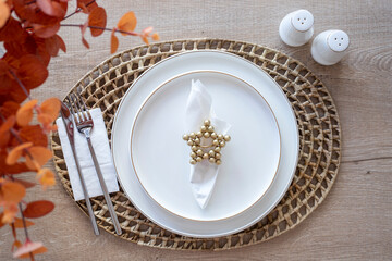 Simple dining table setting with white ceramic plate and silver cutlery over rattan round woven placemat  on wood background. top view, flat lay