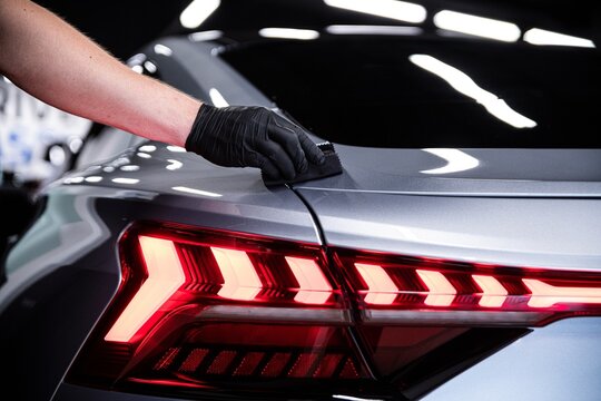 Car detailing studio employee or car wash worker applies a ceramic protective coating to the paint of a silver car