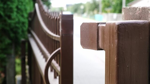 Opening of automatic entrance gate of brown color made of metal. Block fence. Entrance group for cars in the private house. Remote control. Smart home system. Close-up.