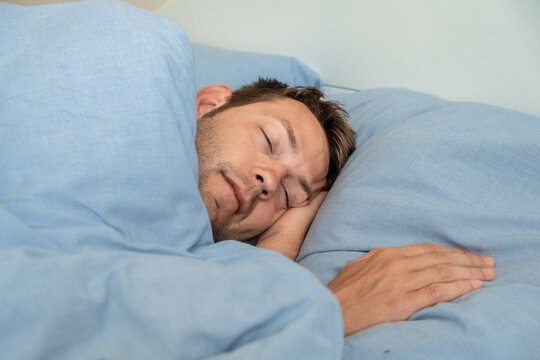 Handsome caucasian man sleeping in bed in the morning rest for healthy wellness in bedroom at home. Tired exhausted male asleep or dreaming in a hotel. Close up