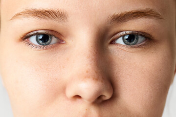 Close-up of female face, eyes, nose. Beautiful young woman with freckles on nose and blue eyes