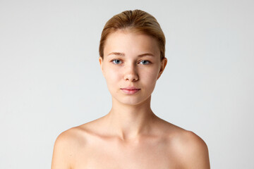 Portrait of beautiful young girl with bare shoulders, well-kept spotless skin isolated over grey...