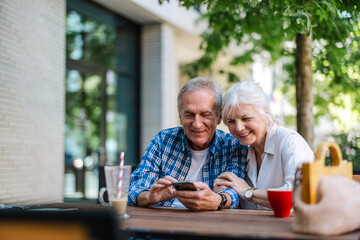 Senior couple sitting at a table in a cafe and using mobile phone
