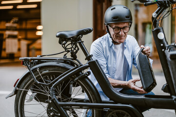 Senior man changing battery on electric bicycle
 - obrazy, fototapety, plakaty