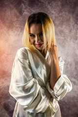 Gorgeous young woman with hairdo in silk robe looking dreamily at camera in home style.