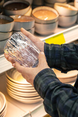 Man holding glass from a shelf in homeware store.