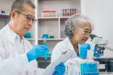 Senior scientists analyzing pharmaceuticals, asian people, senior man and woman, experienced experts in science, conducting pharmaceutical research in modern lab setting with powerful microscope.