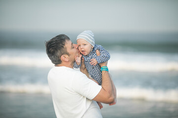 Cheerful young  father with  his  infant son having fun together by seaside, dad throwing up kid in the air