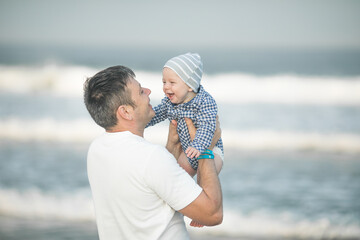 Cheerful young  father with  his  infant son having fun together by seaside, dad throwing up kid in the air