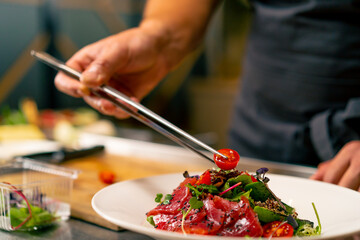 The chef of an Italian restaurant decorates a dish he has prepared in a professional kitchen 