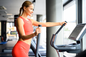 Fototapeta premium Woman exercising in a gym with an elliptical cross trainer