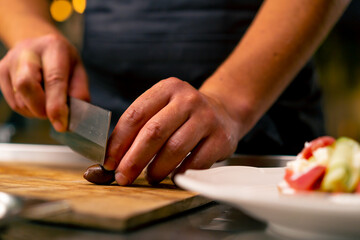 Obraz premium Close-up of a chef cutting olives with a knife while preparing a salad in the kitchen of an Italian restaurant