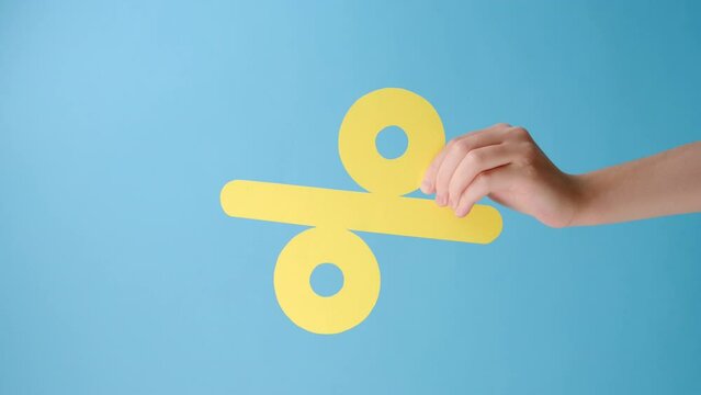 Vertical footage of woman hand holding paper yellow percent mark, presenting big discounts, isolated over blue color background wall in studio with copy space for promotion content or desing