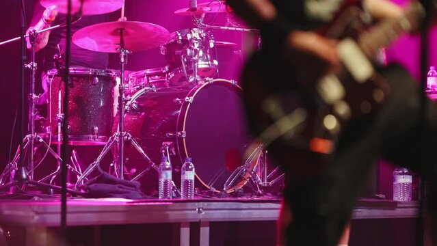 The guitarist of a rock band plays his part at a concert and a drummer playing on the background on the stage