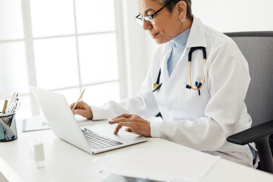 Medical doctor copying patient information from a laptop to a clipboard in her office