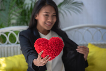 Asian woman show red heart pillow in hands for romantic date at valentine. Girl holding red pillow symbol for show love. happy in love relaxing looking in eye smiling valentine day