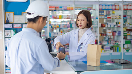 male engineer worker customer buying medication and paying for medicine by credit card. female pharmacist at Drugstore. Professional Pharmacist asian woman at pharma store. Health and wellness center