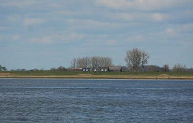 Houses behind the dike of the Elbe river near Wedel in Germany, only the roofs can be seen,  dikes protect the settlements from floods and storms, a vast Nordic looking landscape