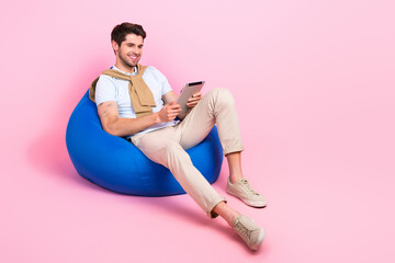 Full body photo of peaceful cheerful man sit comfy bag use tablet empty space ad isolated on pink...