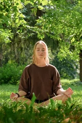 Foto op Canvas meditation Woman meditates in nature outdoor.At ground level, a relaxed woman meditates and breathes while sitting in Lotus pose next to fragrant incense during a yoga class in the garden © shintartanya