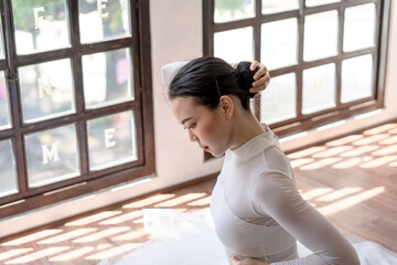 Asian girl ballet dancer preparing fixing her hair into a bun during ballet class. ballerina adjusting her hair 
